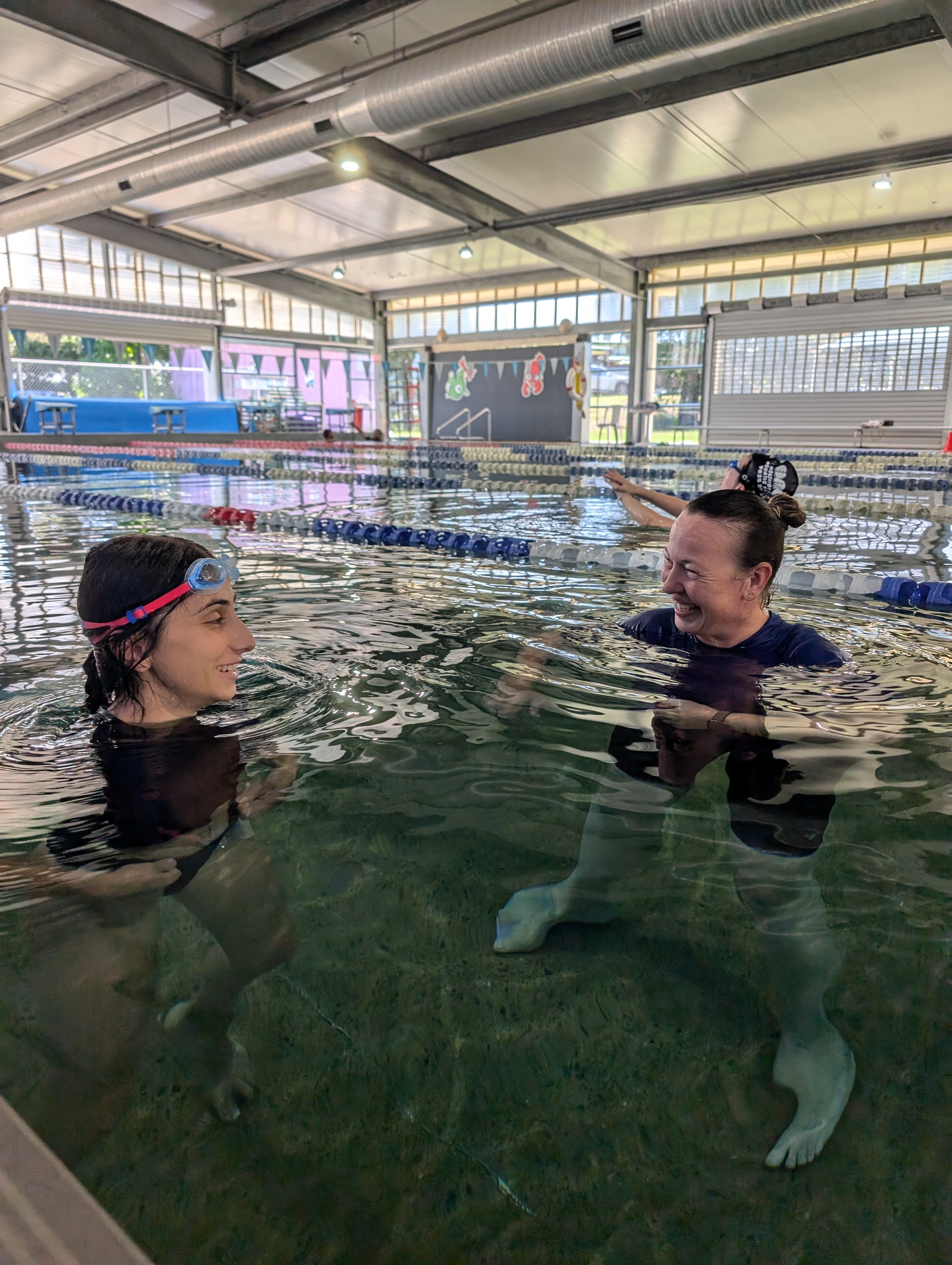 A swimming teacher and an adult student smiling and chatting in the pool during a swimming lesson