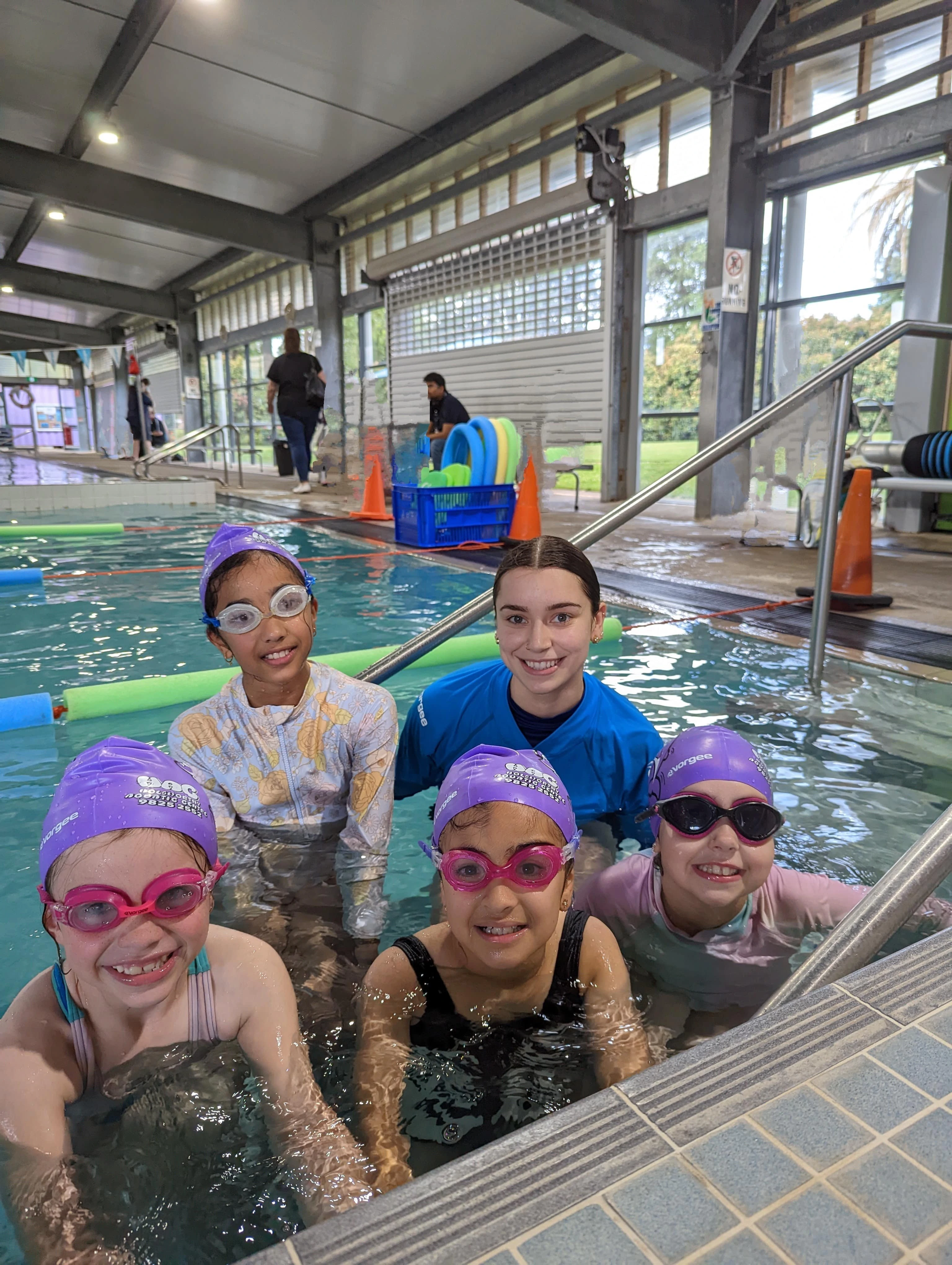 Four Dolphin level swimmers sitting on pool steps with their instructor during a swimming lesson