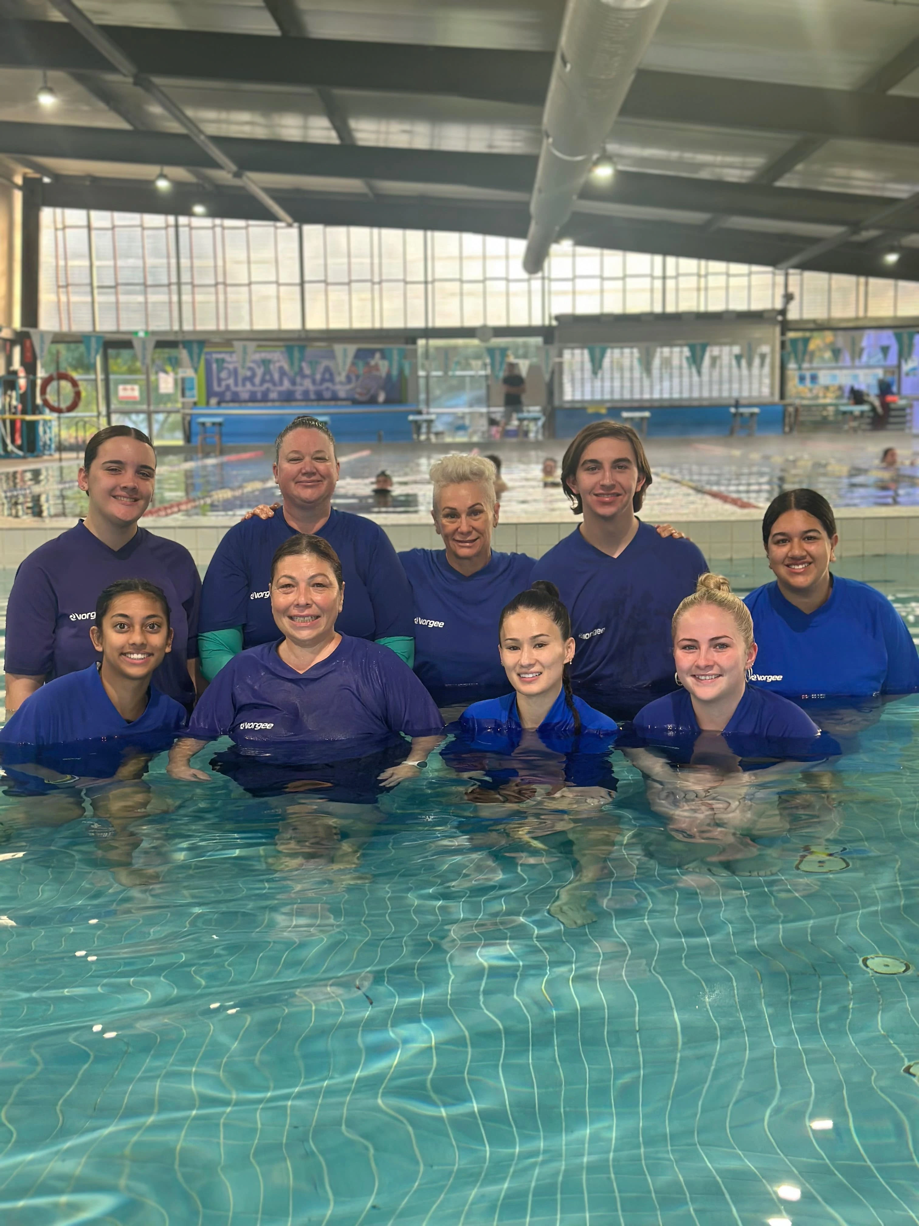 Swim teachers standing together in the pool, smiling and facing the camera.